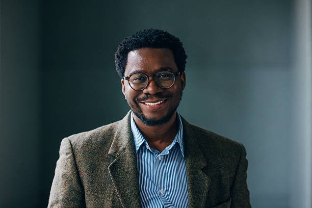 A confident man in a tweed blazer smiling warmly, exuding professionalism and approachability in a modern indoor setting.
